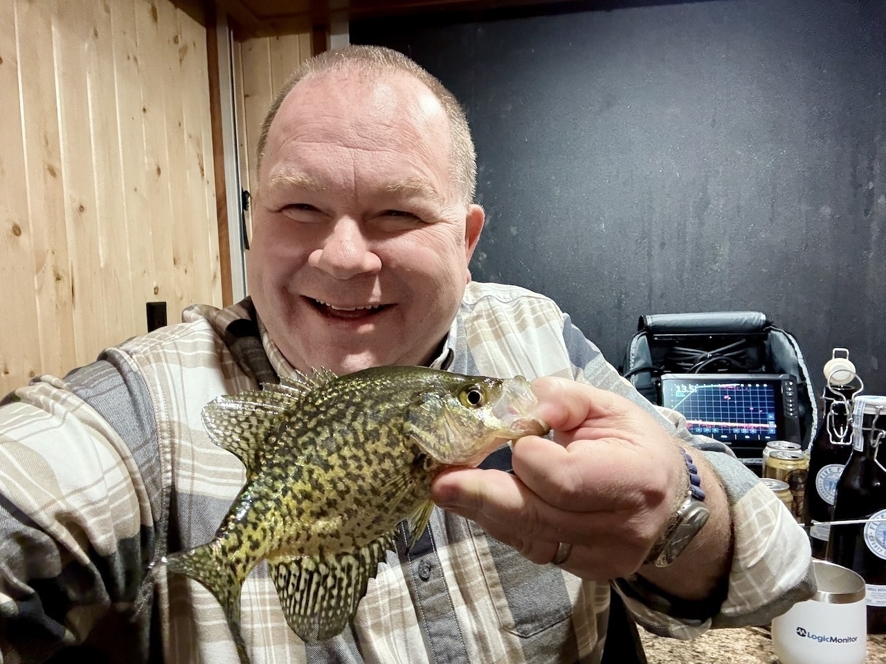 A person is smiling and holding a fish inside a room with wood-paneled walls.