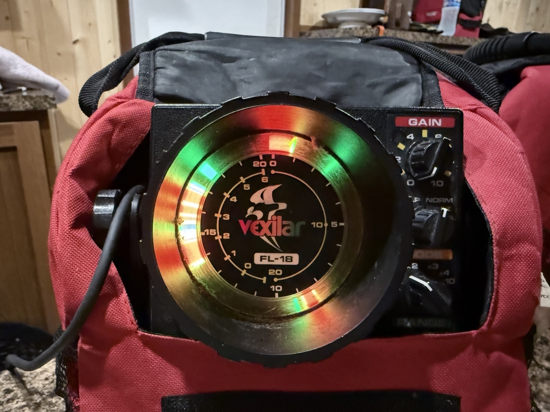 A Vexilar FL-18 fish finder is displayed, showing colorful sonar readings, surrounded by a red and black case.